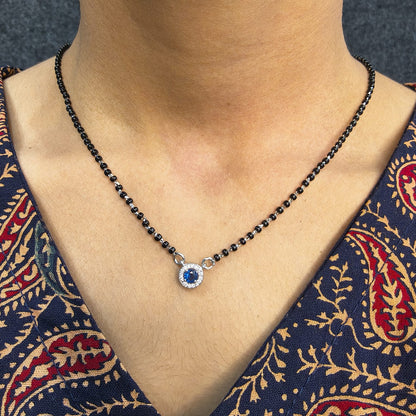 Necklace with a blue gemstone pendant on a person wearing a patterned garment.