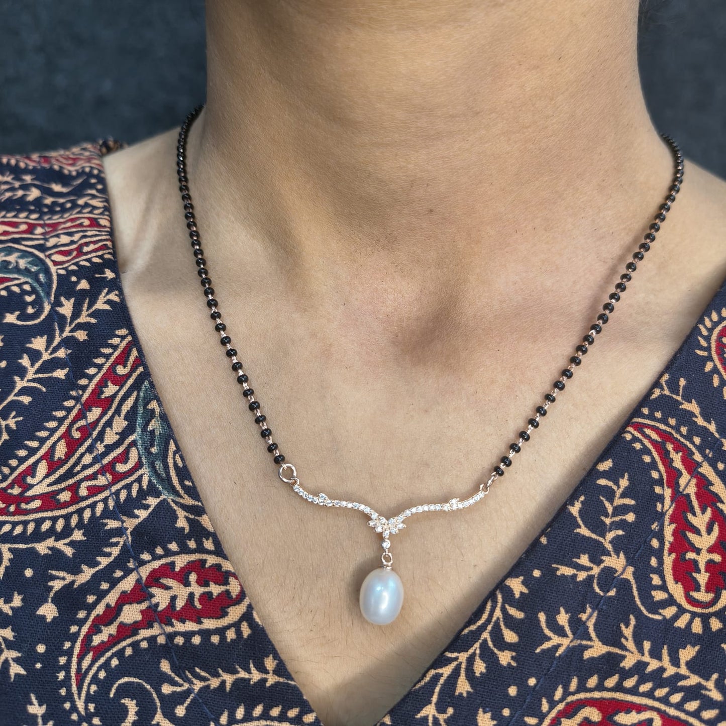 Necklace with a pearl pendant worn by a person against a patterned garment.