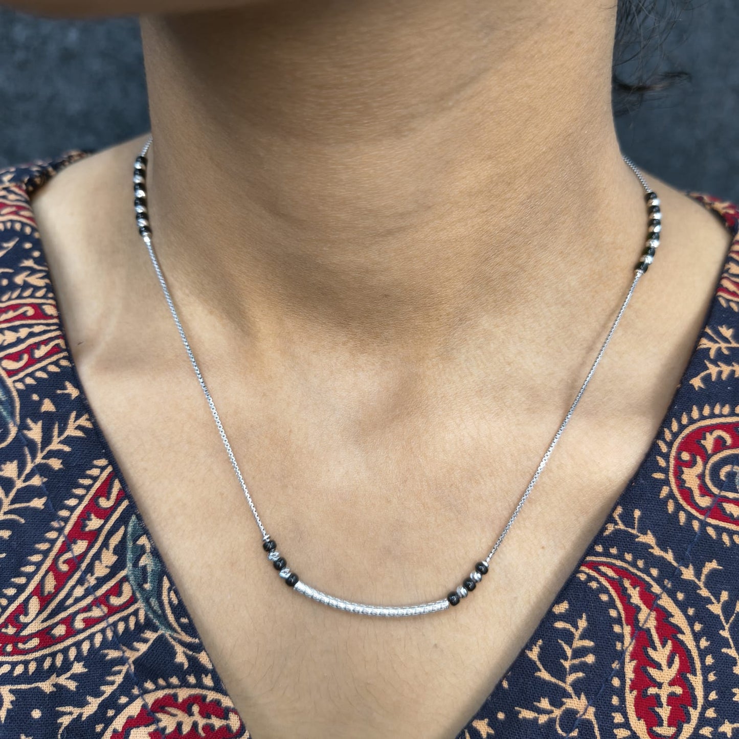 Necklace with black beads worn by a person in a patterned garment