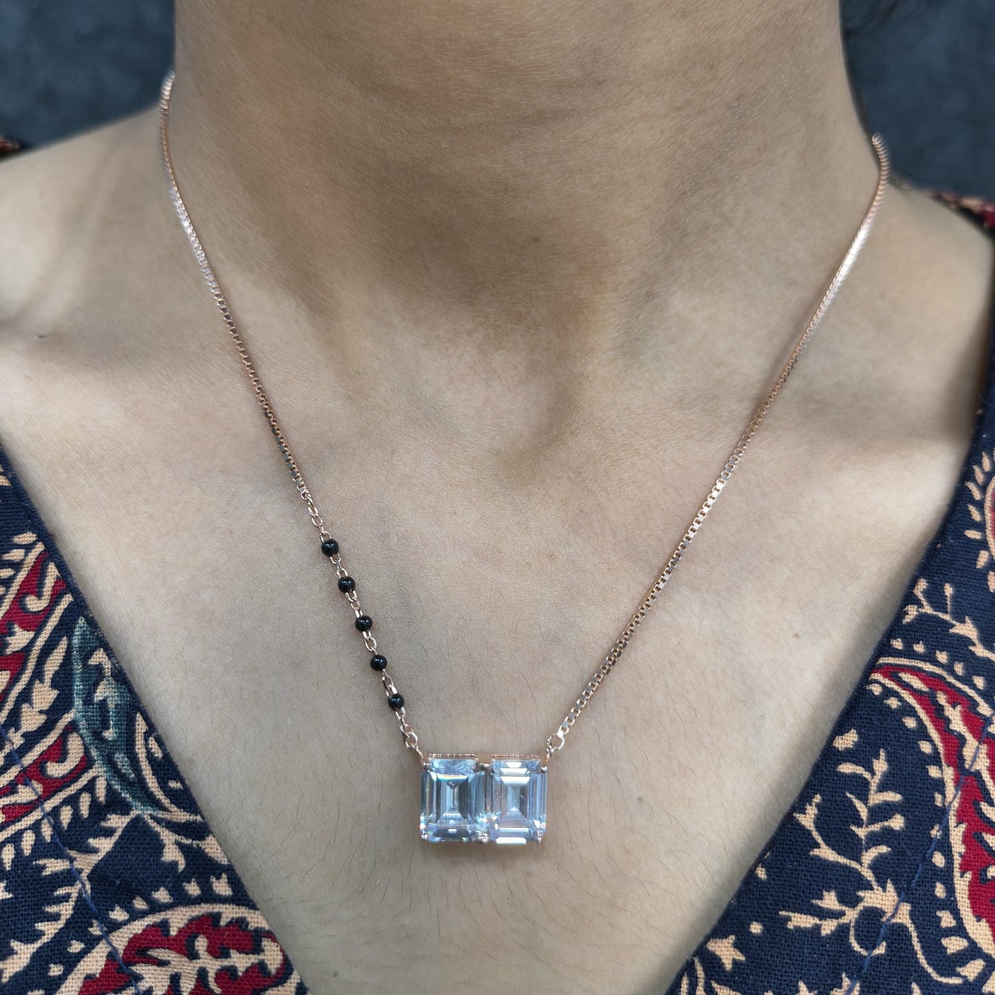Necklace with a blue gemstone pendant on a person wearing a patterned top.