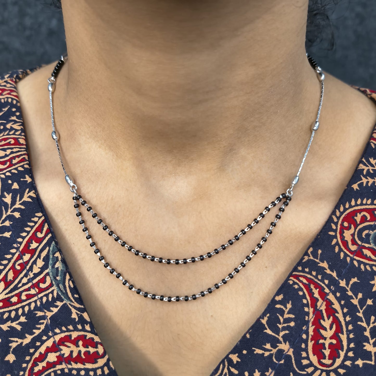 Necklace with black beads on a person wearing a patterned garment