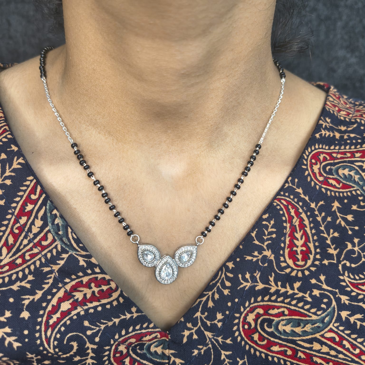 Necklace with black beads and silver pendant on a person wearing a patterned garment.
