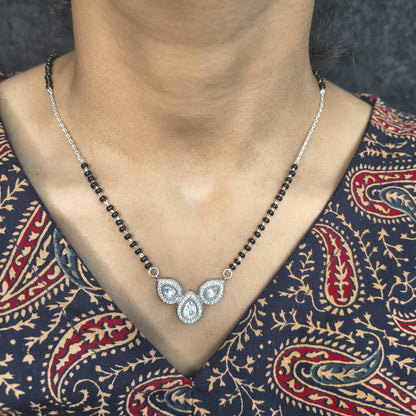 Necklace with black beads and silver pendant on a person wearing a patterned garment.