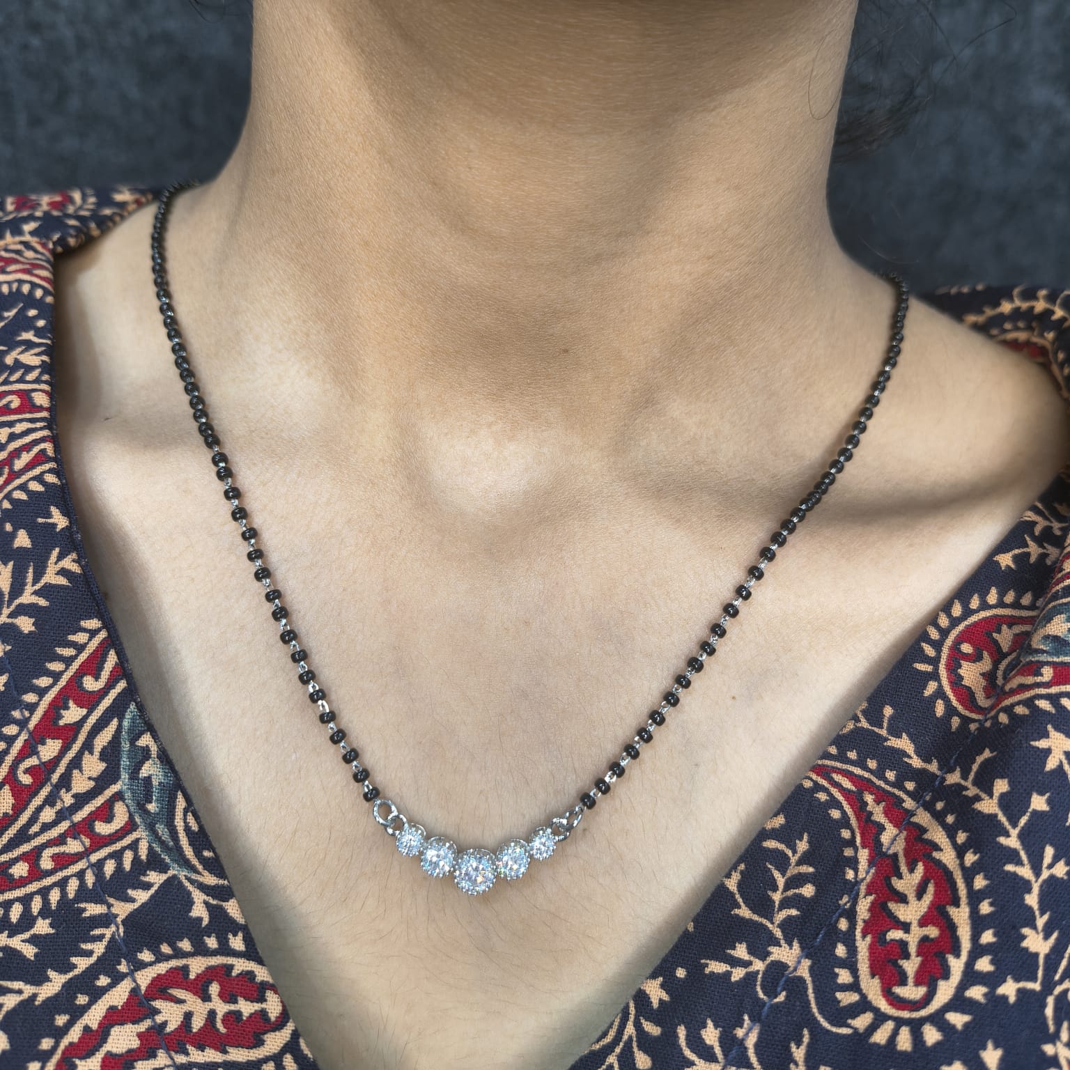 Necklace with blue gemstones worn by a person against a patterned fabric background