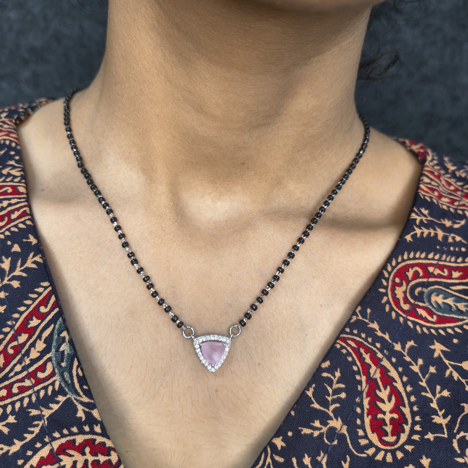 Necklace with a pink gemstone pendant worn by a person in a patterned garment.