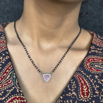 Necklace with a pink gemstone pendant worn by a person in a patterned garment.