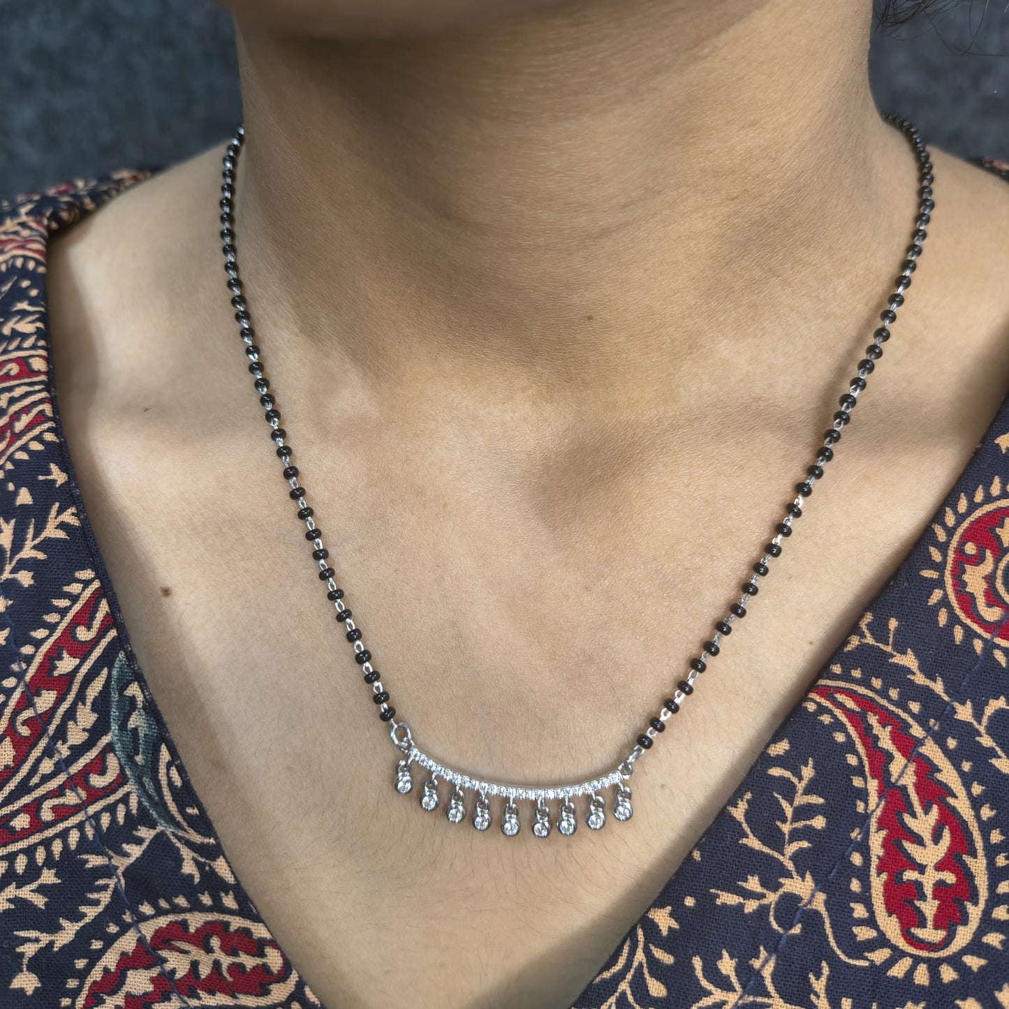 Necklace with small droplet pendants on a person wearing a patterned garment.