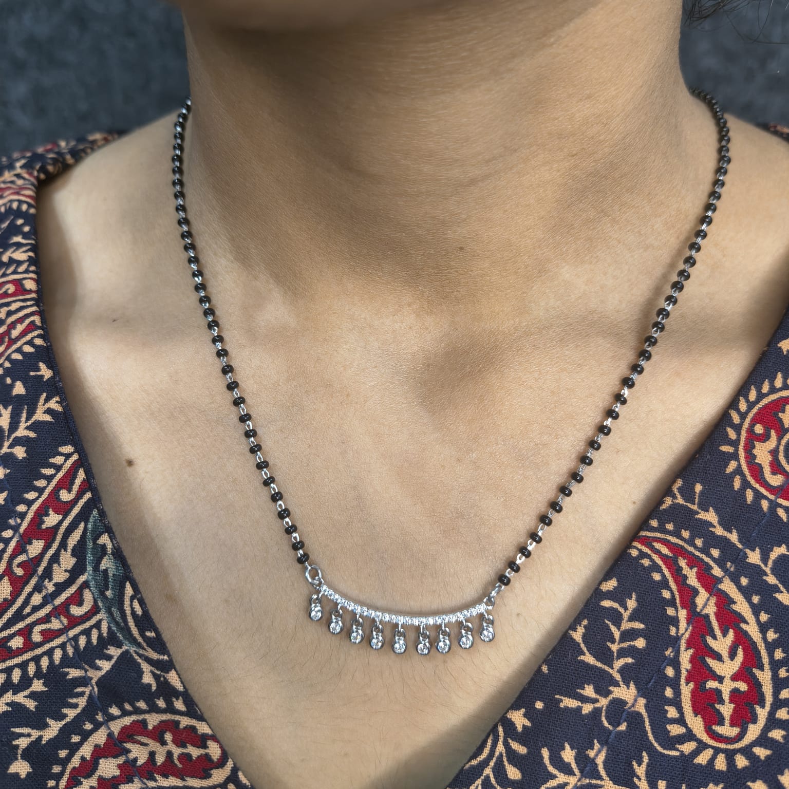 Necklace with small droplet pendants on a person wearing a patterned garment.