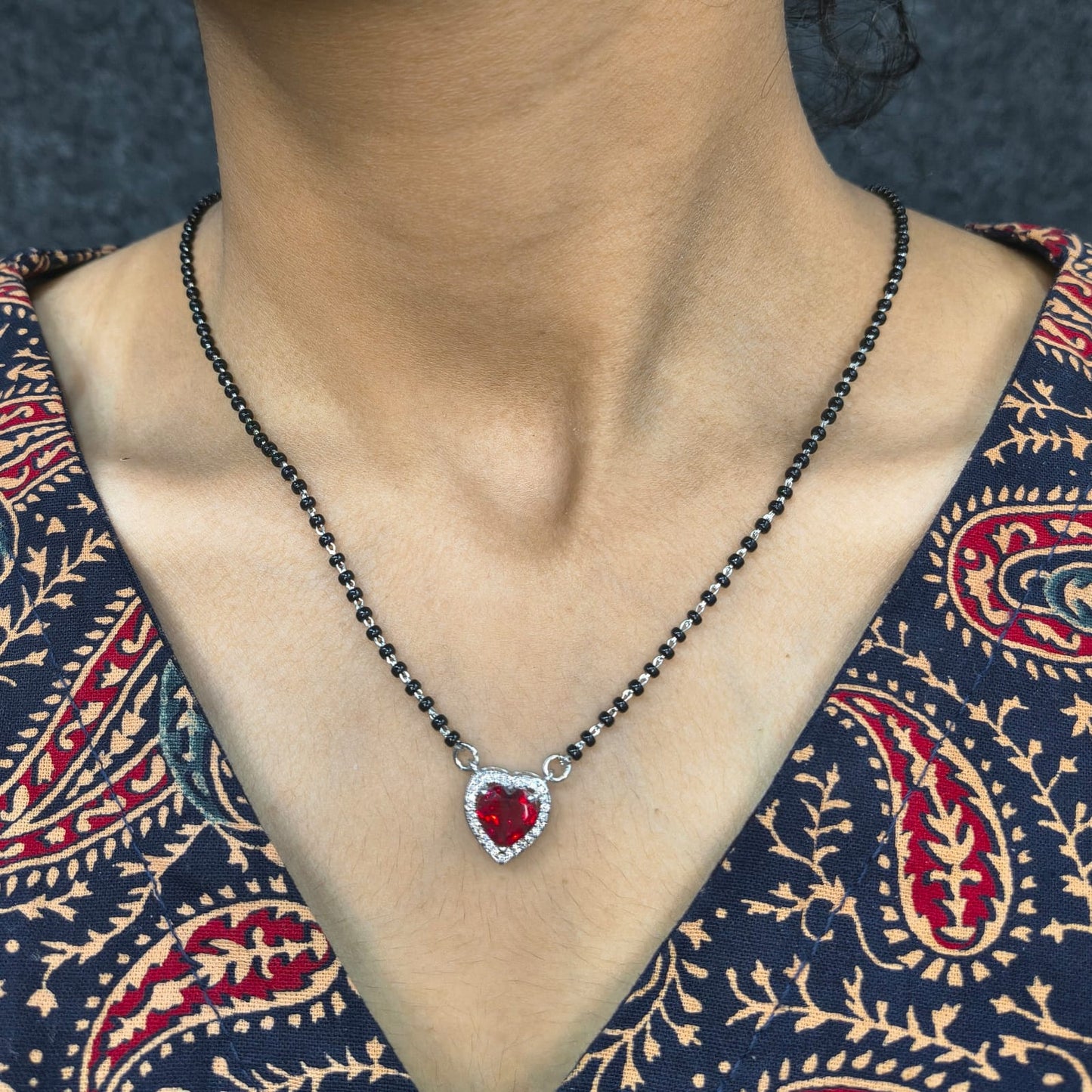 Necklace with a red heart pendant worn by a person in a patterned garment.