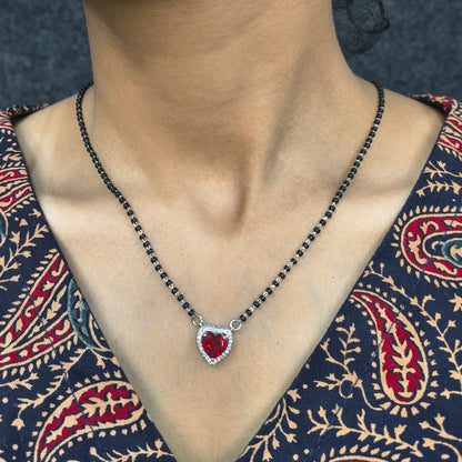 Necklace with a red heart pendant worn by a person in a patterned garment.