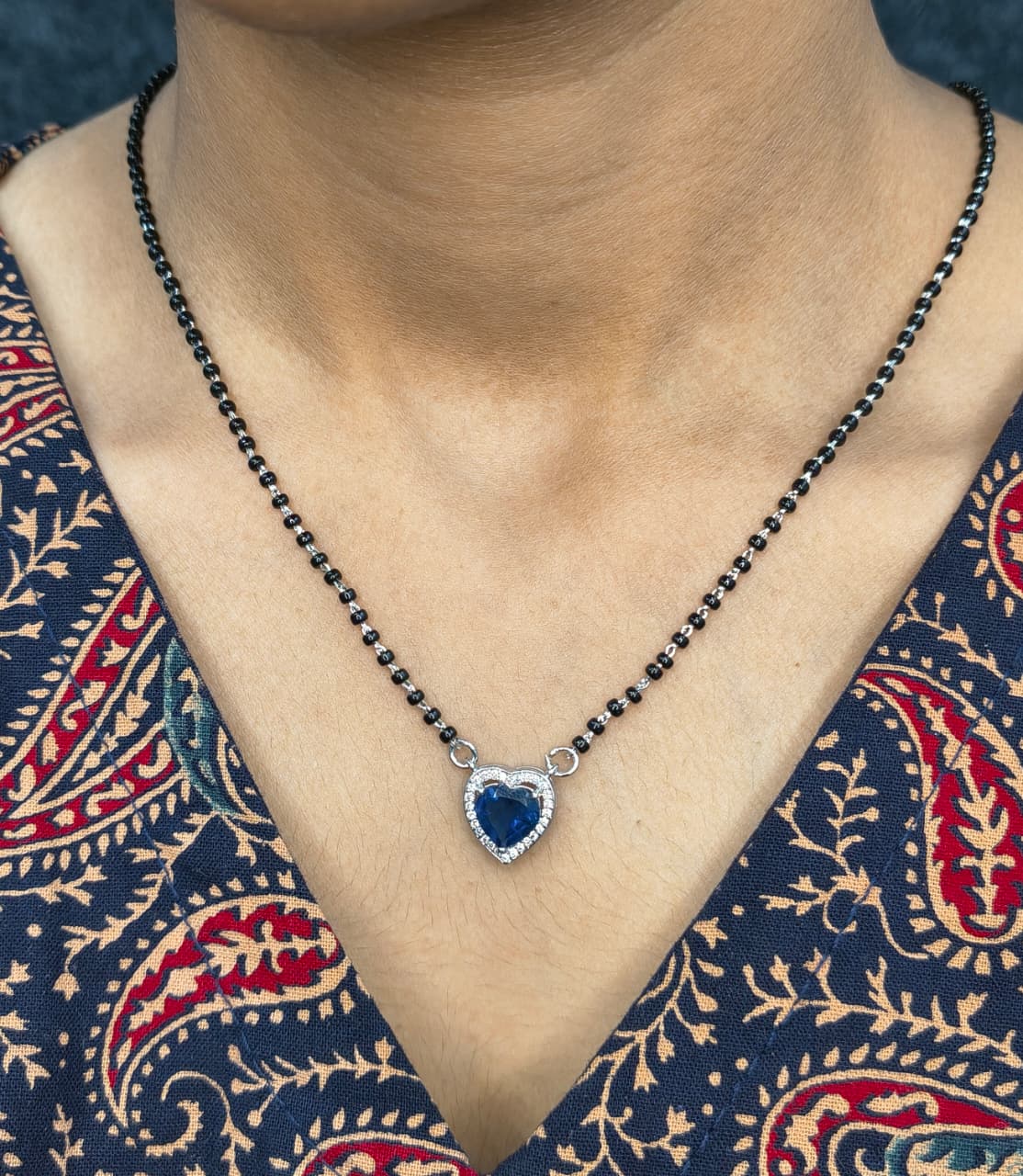 Necklace with a blue heart pendant worn by a person in a patterned garment.
