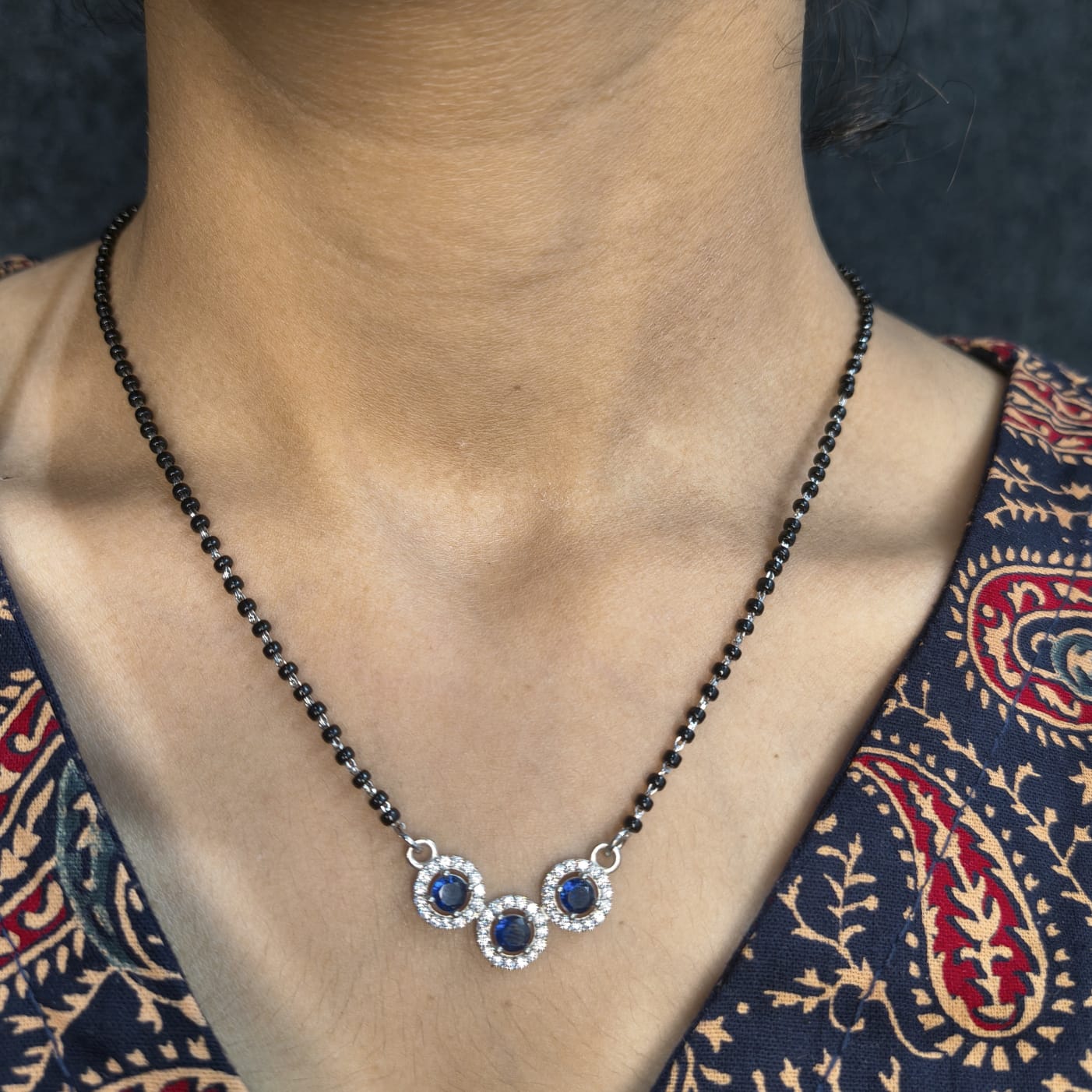Necklace with blue stones worn by a person against a patterned fabric background