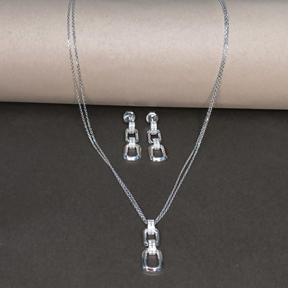 Silver necklace and earrings set on a dark surface with a cardboard roll in the background.