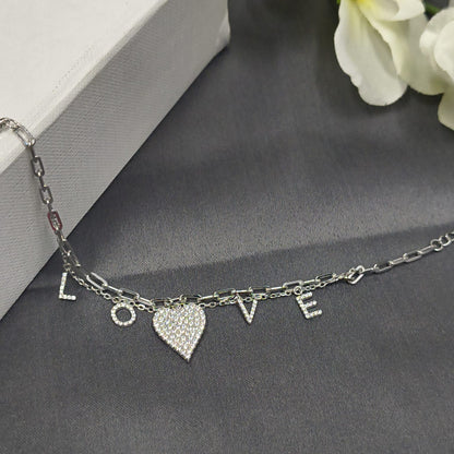 Silver bracelet with heart charm and 'LOVE' letters on a gray surface with white flowers.
