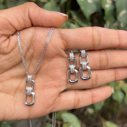 Silver chain necklace and earrings held in a hand with a natural background