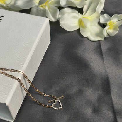 Gold chain necklace with a heart pendant on a gray surface with flowers in the background