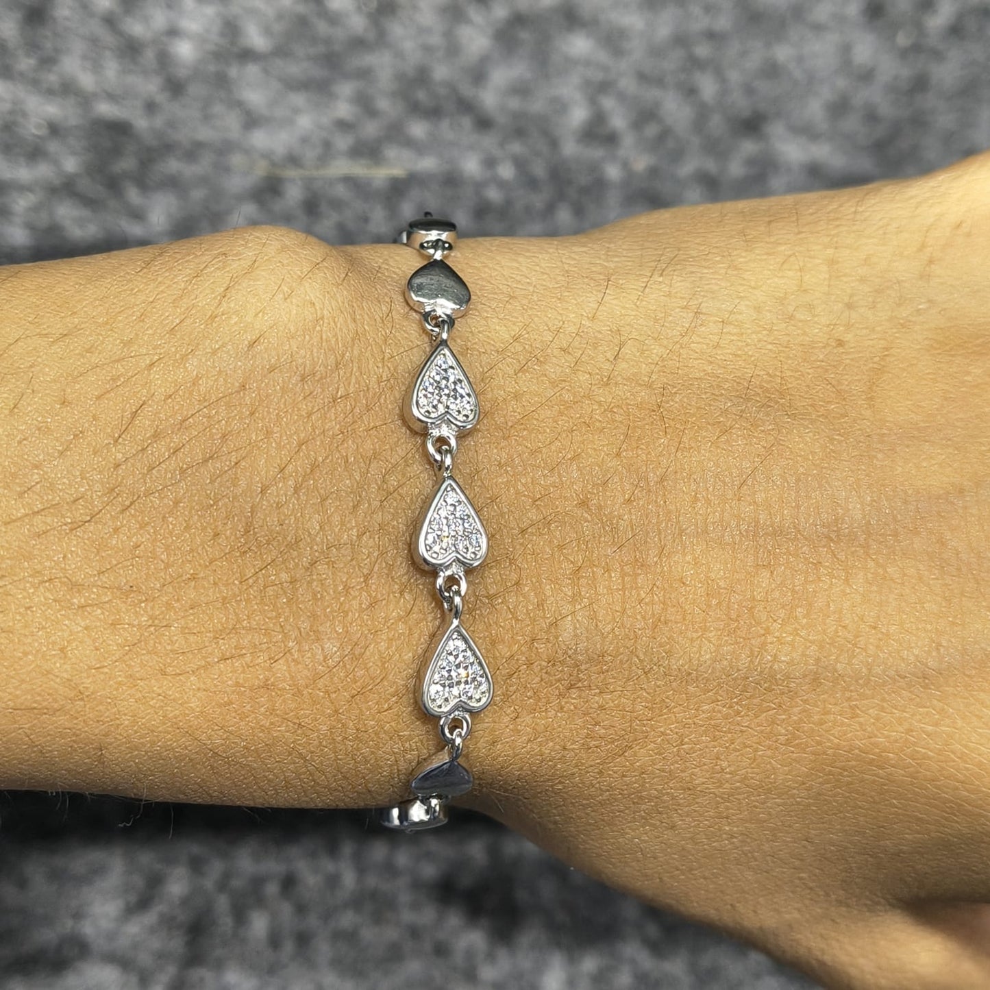 Silver bracelet with heart-shaped charms on a wrist against a gray background