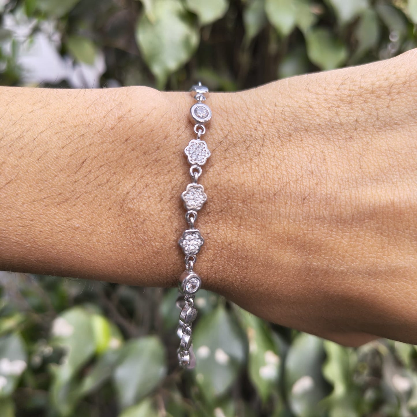 Silver bracelet on a wrist with a blurred green leafy background