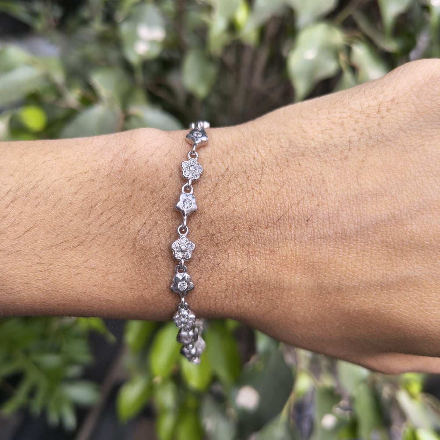 Silver bracelet on a wrist with a green leafy background