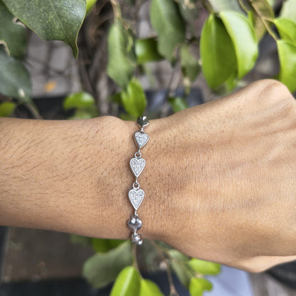 Silver heart-shaped bracelet on a wrist with a blurred green leafy background