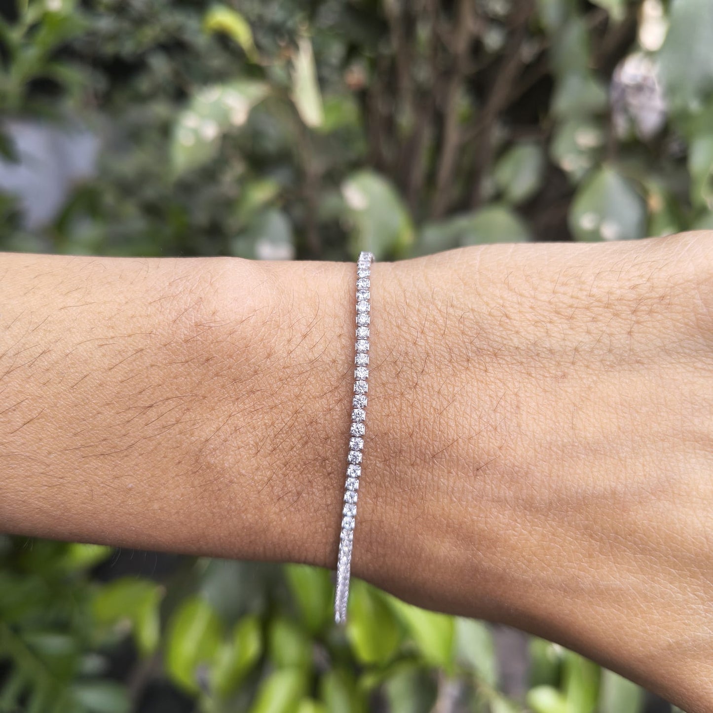 Silver bracelet on a wrist with a blurred green leafy background