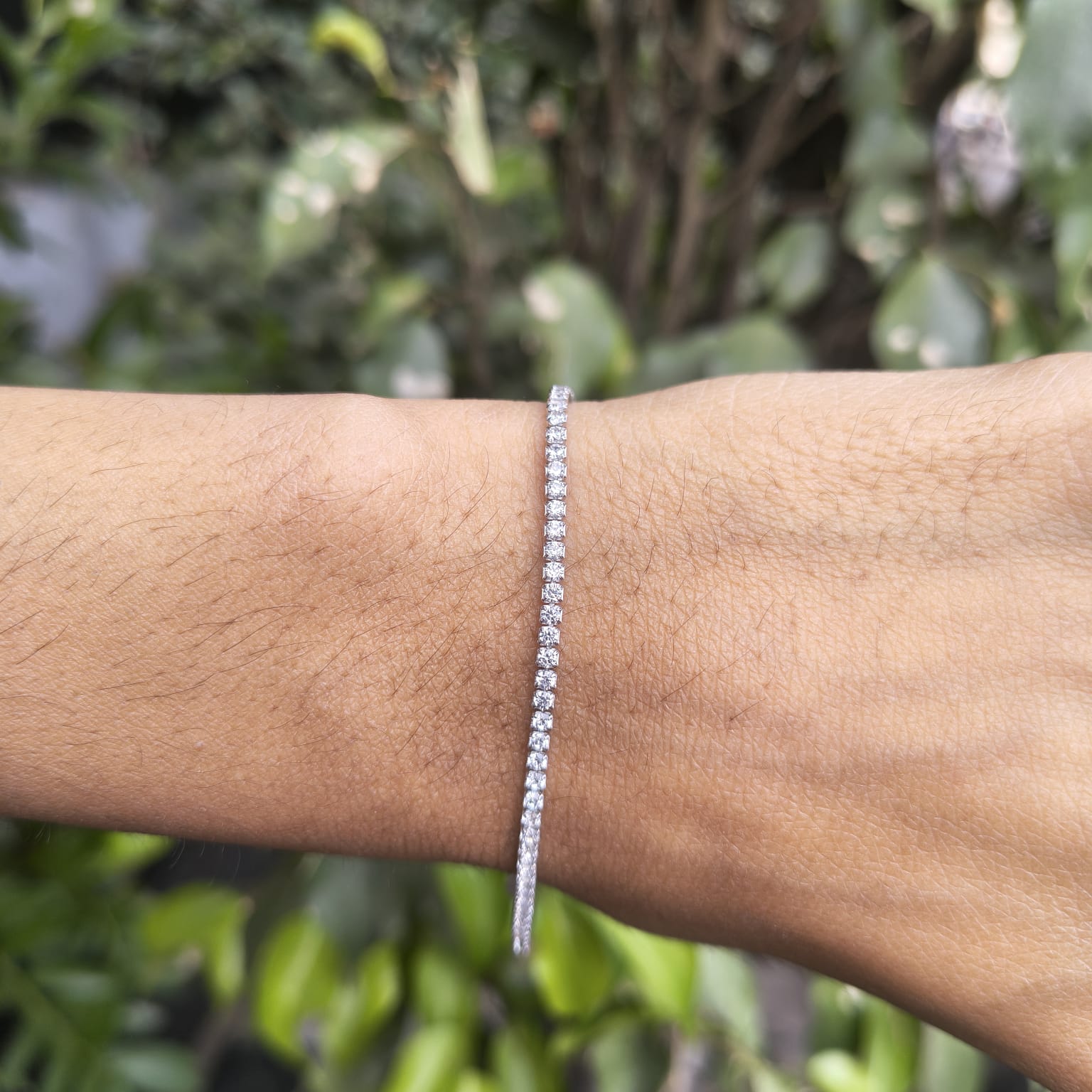 Silver bracelet on a wrist with a blurred green leafy background
