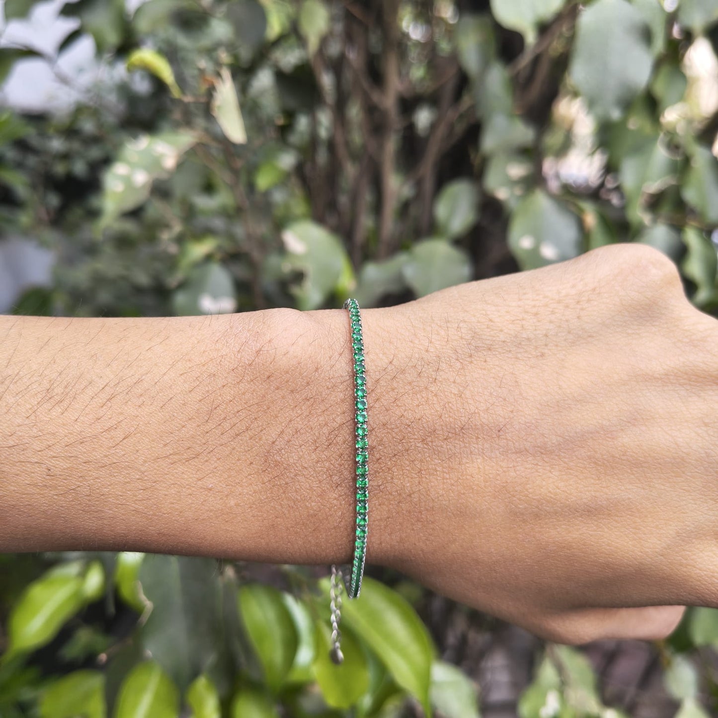 Green beaded bracelet on a wrist with a blurred green leafy background