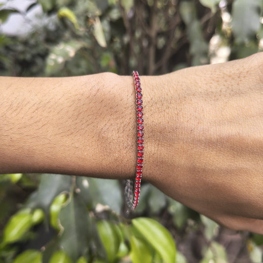 Red beaded bracelet on a wrist with a blurred green leafy background