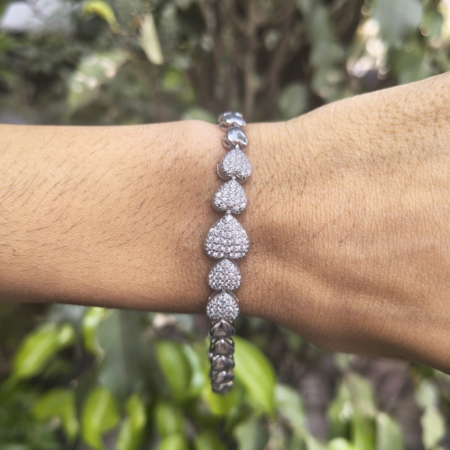 Silver bracelet on a wrist with a blurred green background