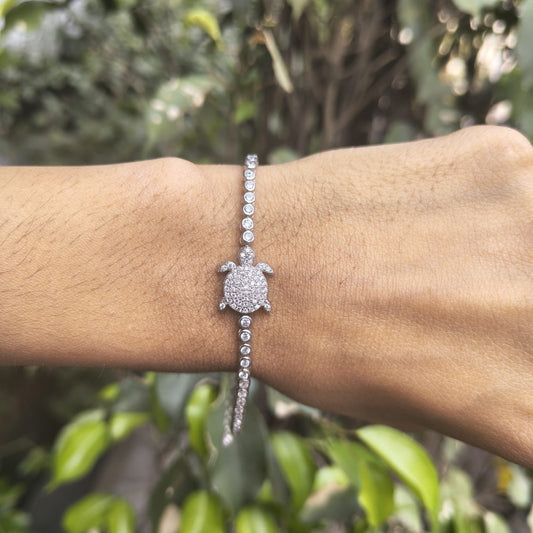 Silver turtle bracelet on a wrist with a blurred green background