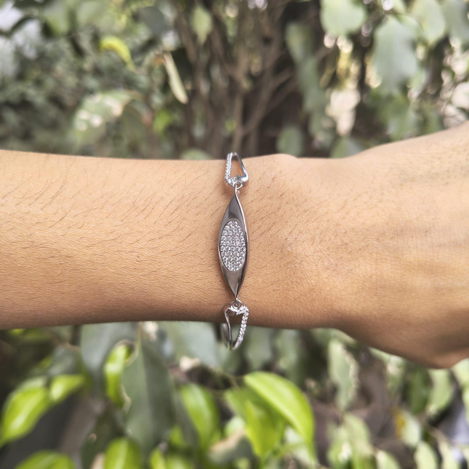 Silver bracelet with a diamond-like stone on a wrist against a blurred green background