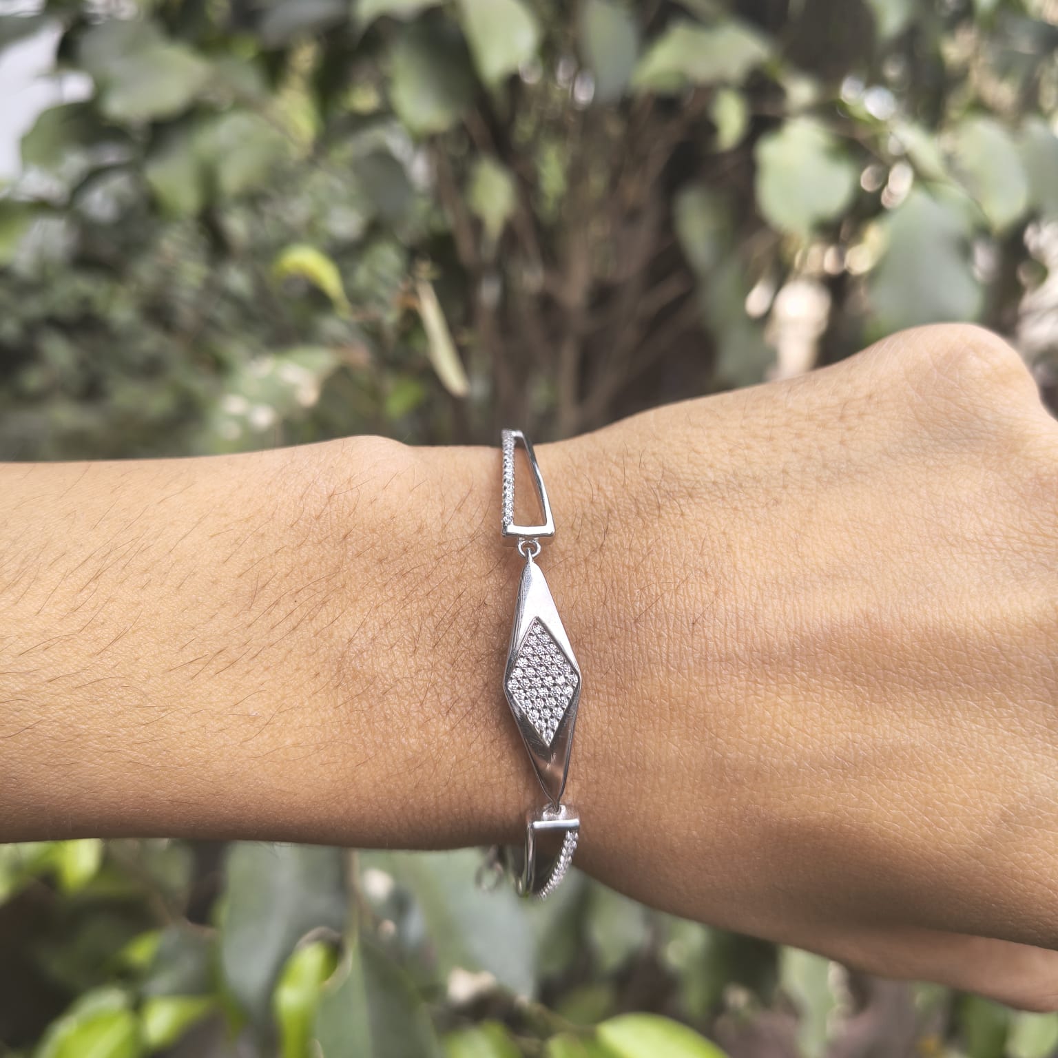 Silver bracelet on a wrist with a blurred green background