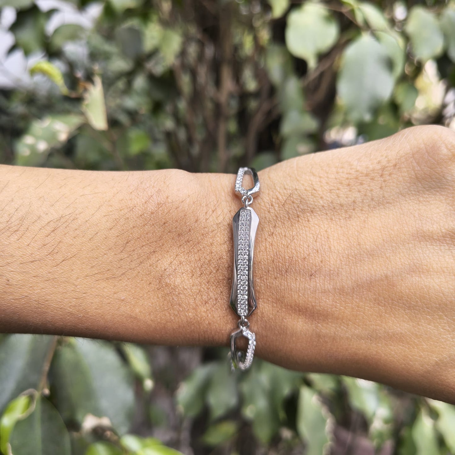 Silver bracelet on a wrist with a blurred green leafy background