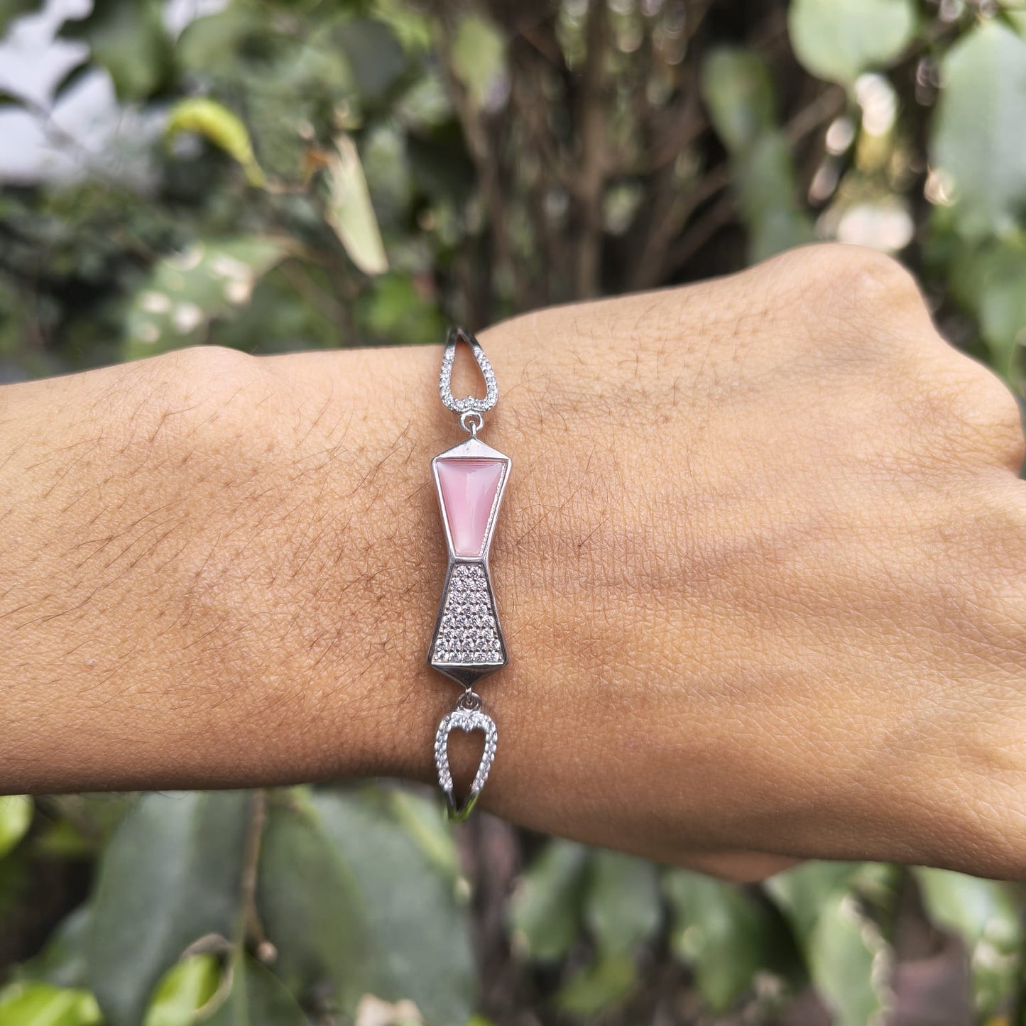 Bracelet with pink and silver design on a wrist against a blurred green background