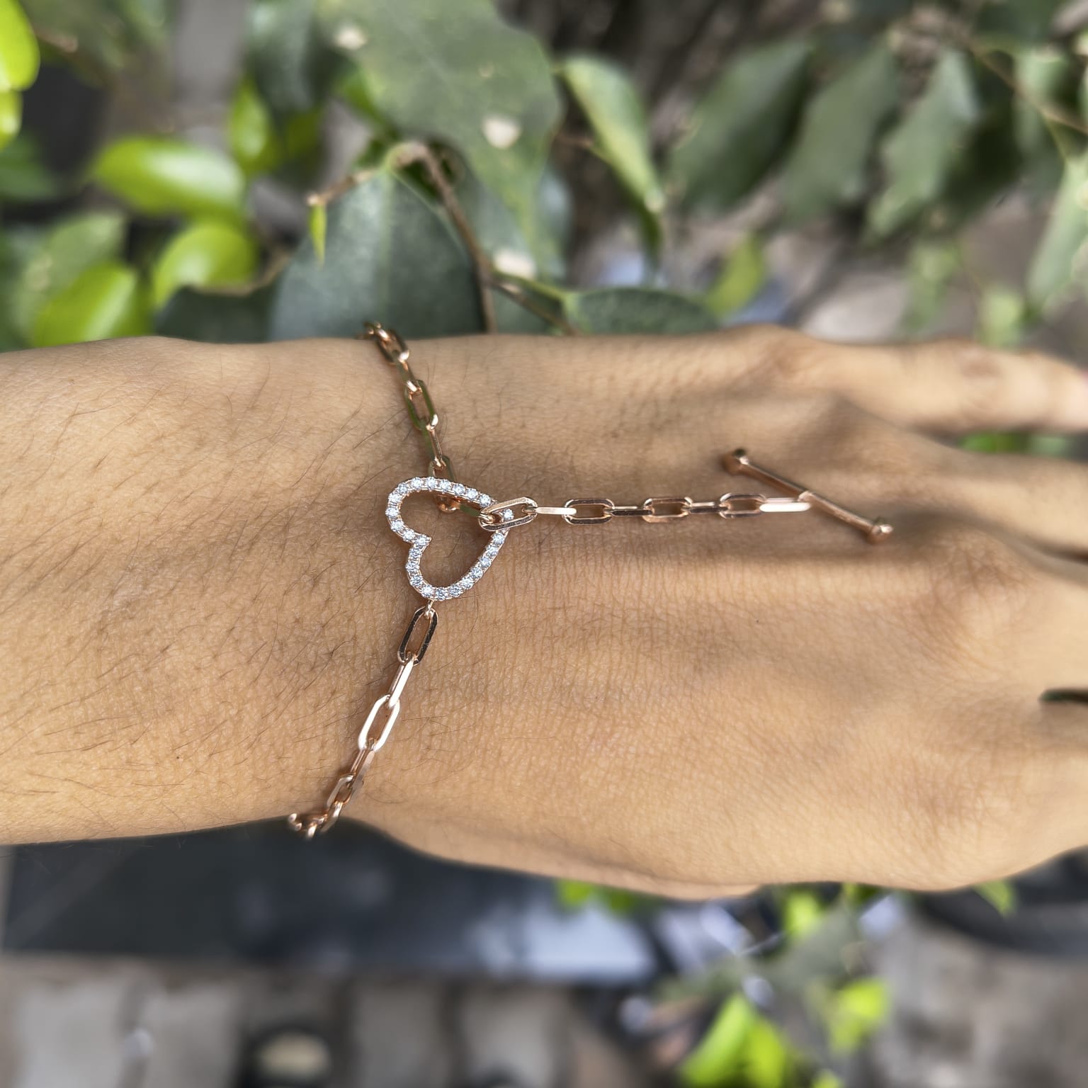 Bracelet with a heart charm on a wrist against a blurred green background