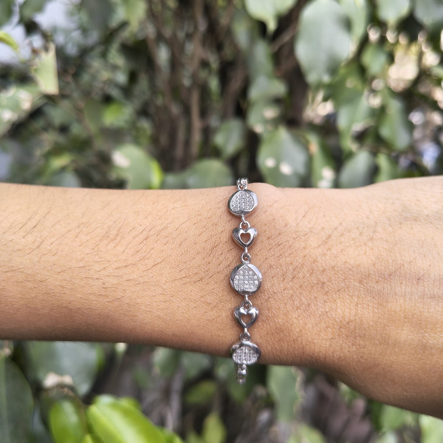 Silver bracelet on a wrist with a blurred green leafy background