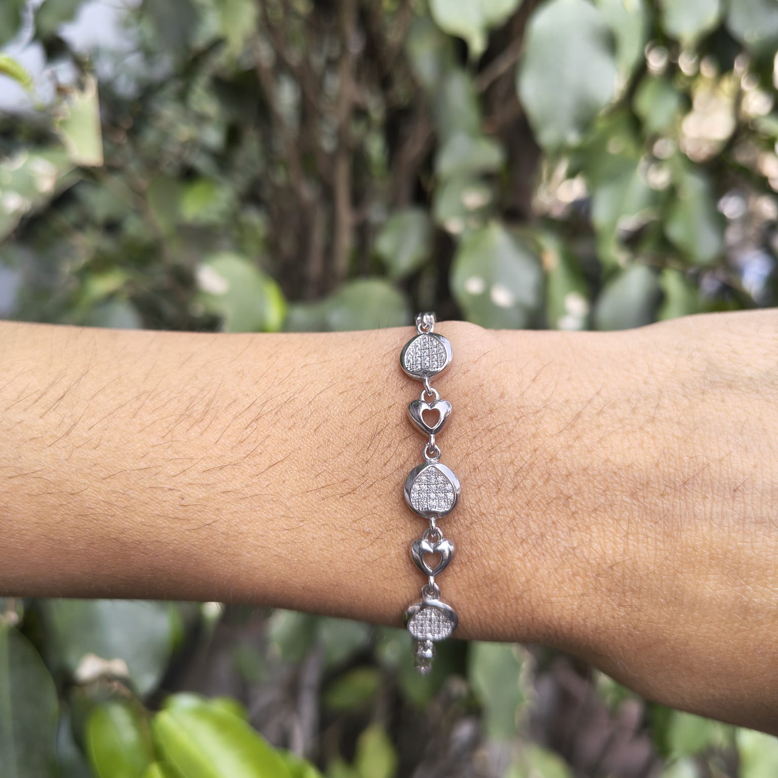 Silver bracelet on a wrist with a blurred green leafy background