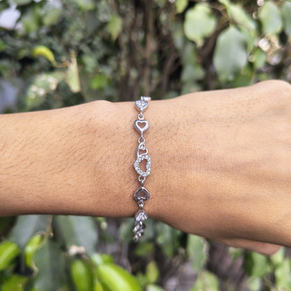 Silver bracelet with heart and circular designs on a wrist against a blurred green background