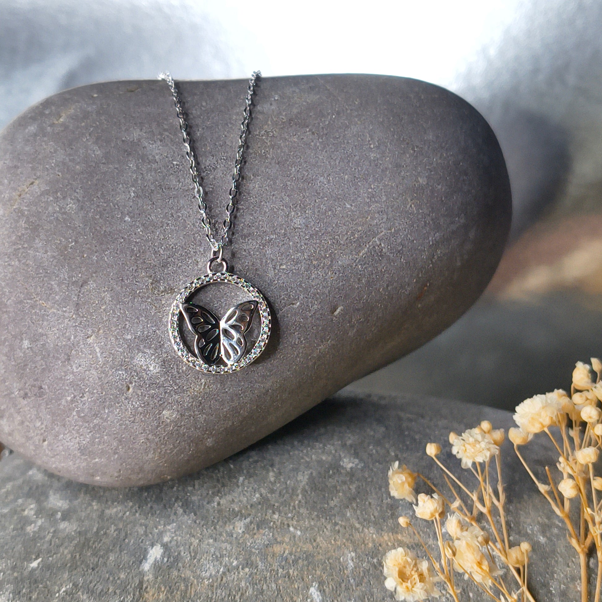 Silver necklace with a pendant on a stone surface with dried flowers.