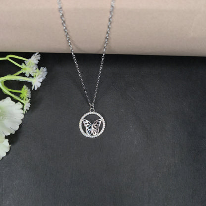 Silver butterfly pendant necklace on a dark surface with white flowers