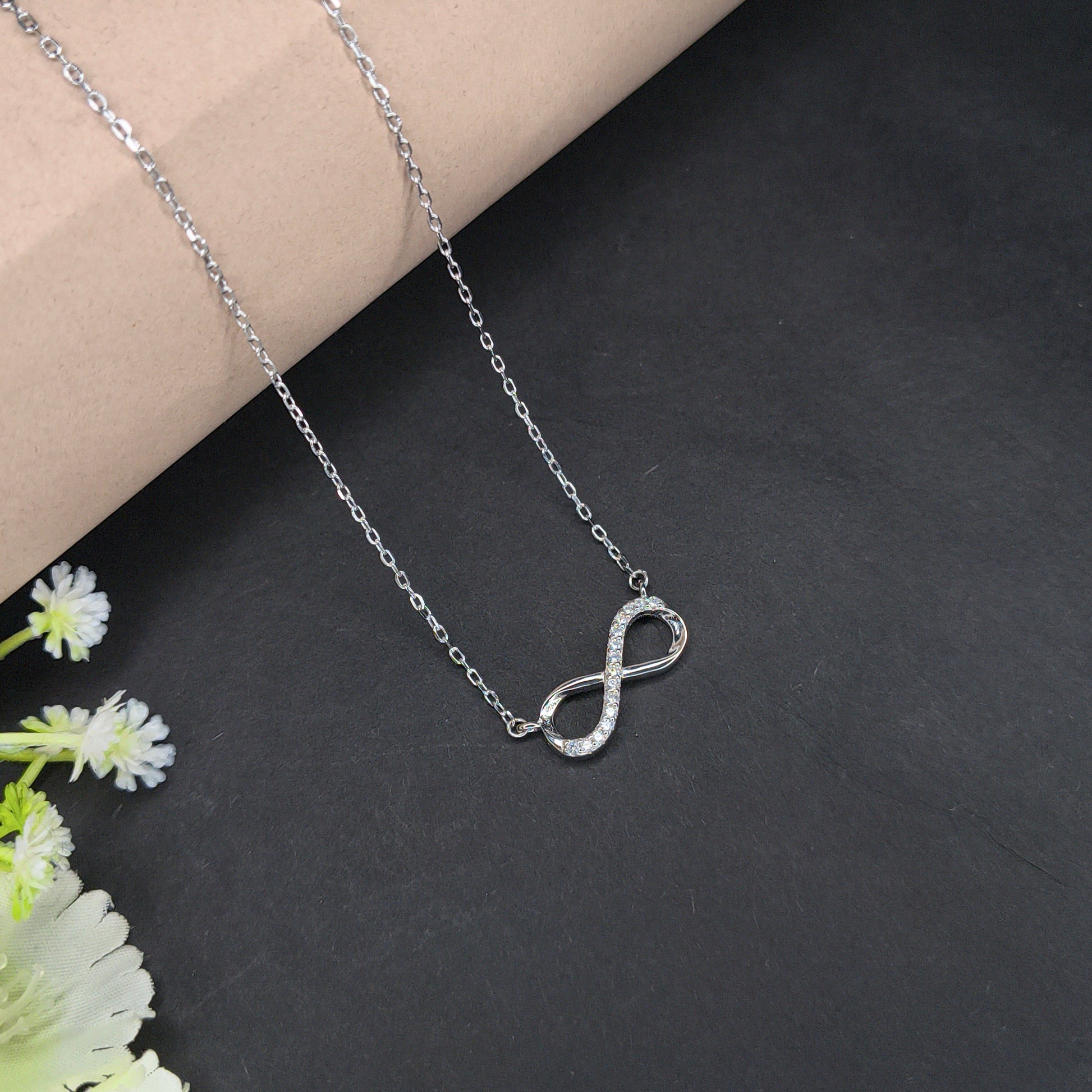Silver infinity necklace on a dark surface with flowers