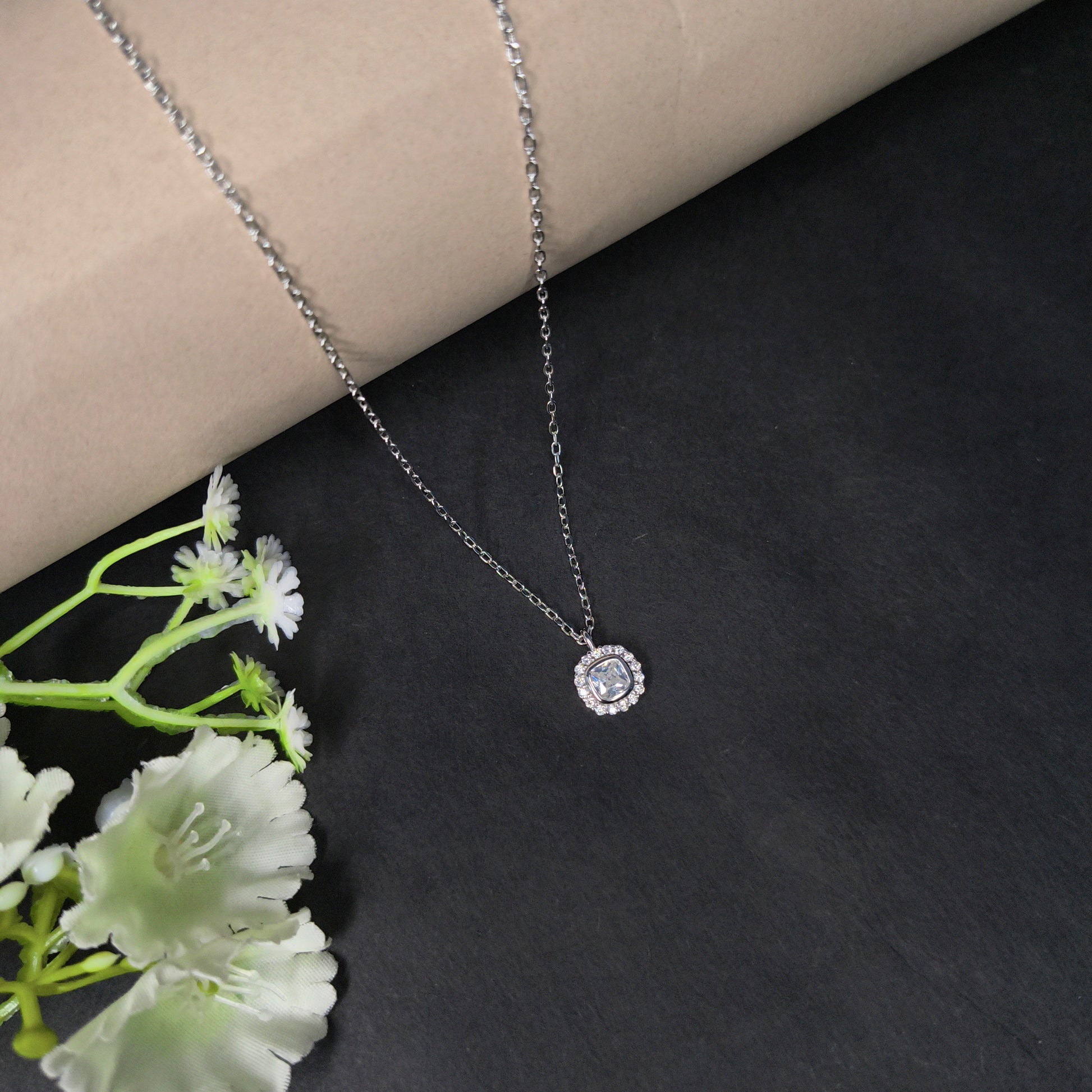Silver necklace with a pendant on a dark surface with white flowers.
