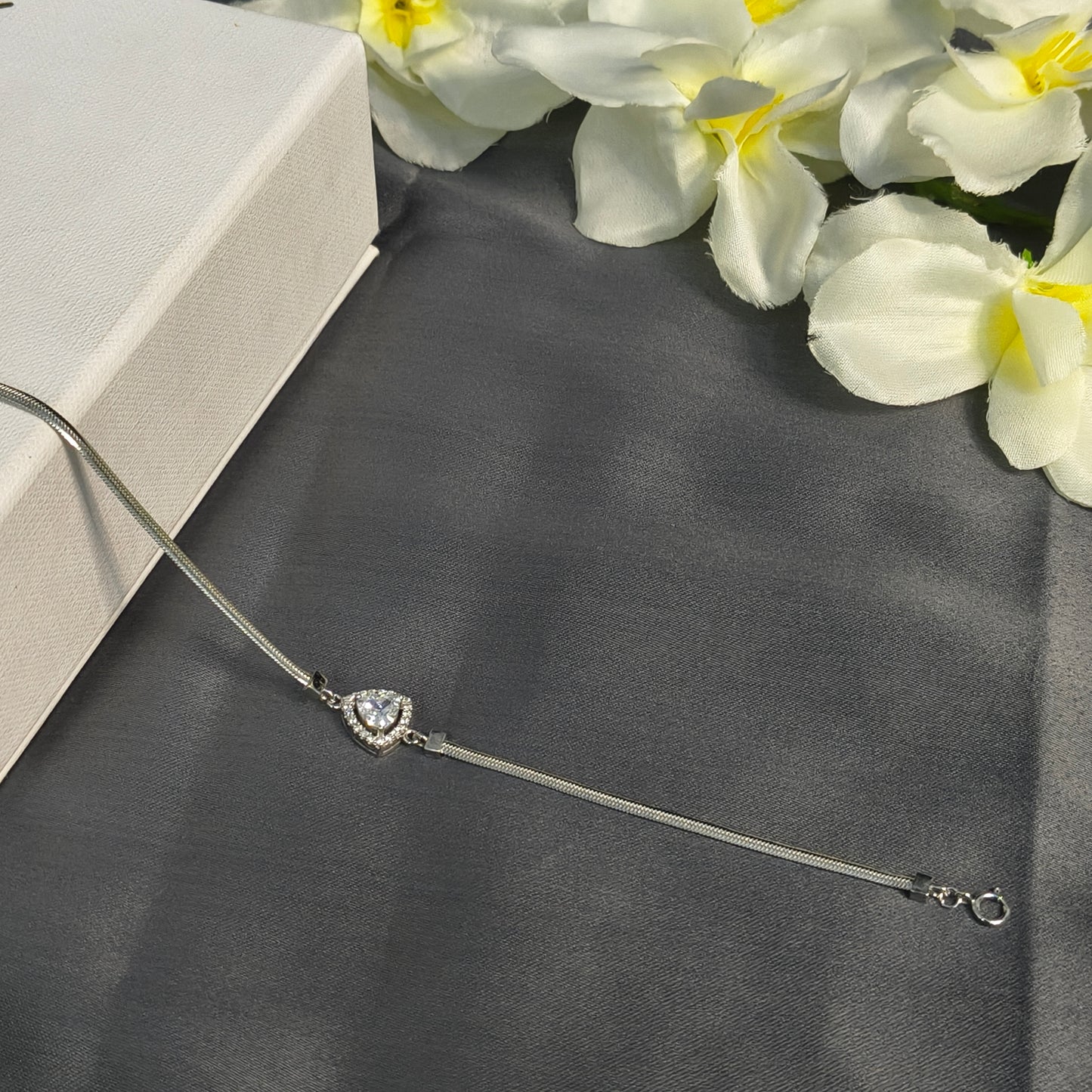 Silver bracelet with a heart charm on a dark surface with yellow flowers in the background