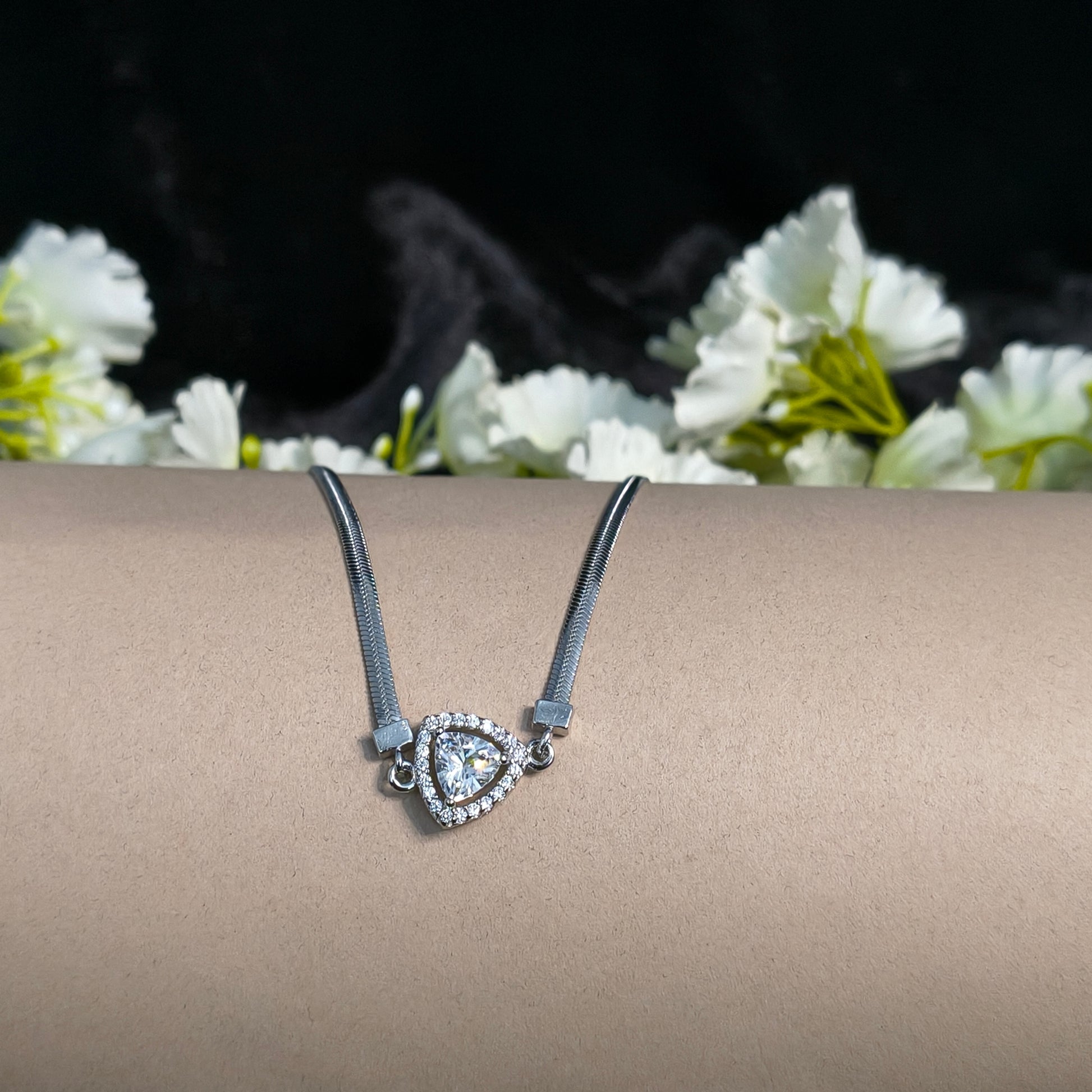 Silver necklace with a heart-shaped pendant on a beige surface with white flowers in the background