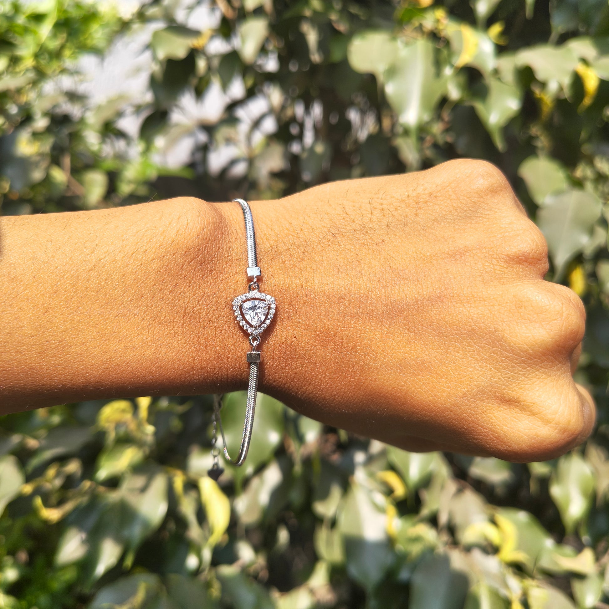 Silver bracelet with a heart-shaped pendant on a wrist against a green leafy background